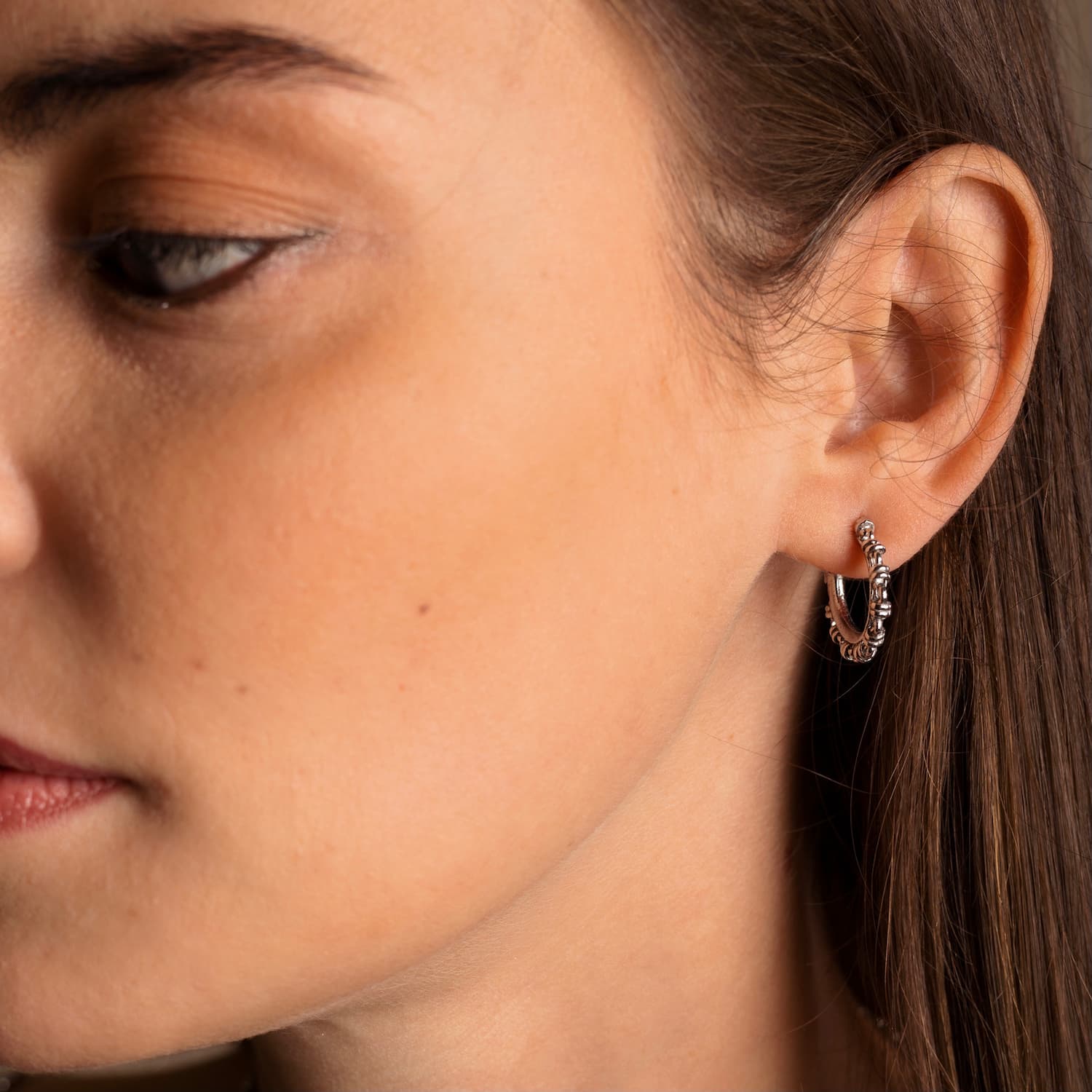 A closeup of a model wearing silver hoop earrings designed and hand-crafted by DelBrenna Italian Jewelers in Tuscany. The earrings are designed based on the iconic Links collection of DelBrenna silver chains, necklaces, rings, and bracelets. 