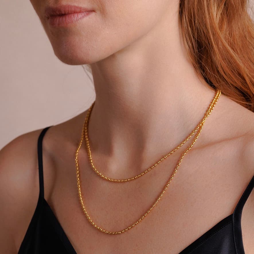 A right-side, close-up view of a model wearing two delicate, hand-crafted 2MM gold chains in two different lengths: a short, 16-18” gold chain necklace and a 20-22” gold necklace - both gold necklaces are crafted by DelBrenna Italian Jewelry designers in Tuscany.