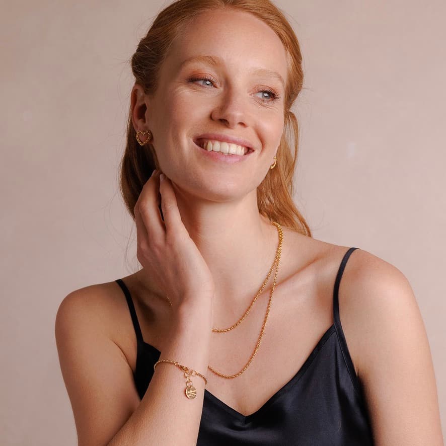 A model wearing two delicate, hand-crafted 2MM gold chains in two different lengths:  a short, 16-18” gold chain necklace and a 20-22” gold necklace with matching gold heart earrings and a gold bracelet with a gold charm. All jewelry is hand-crafted by DelBrenna Italian Jewelry designers in Tuscany. 