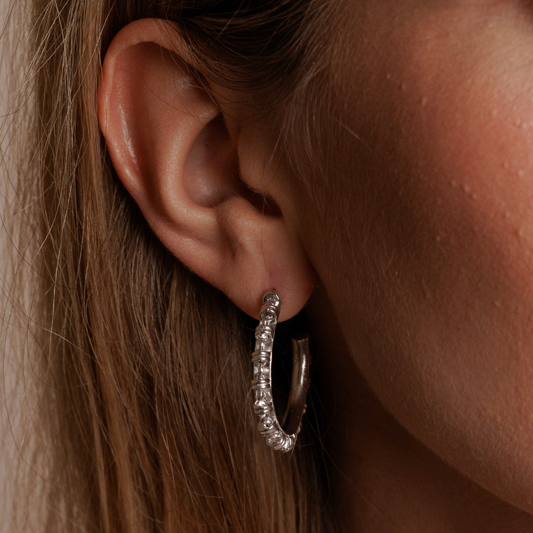 A closeup of a model wearing large silver hoop earrings with a chain design from DelBrenna Italian jewelry design. The earrings are hand-crafted in Tuscany. 