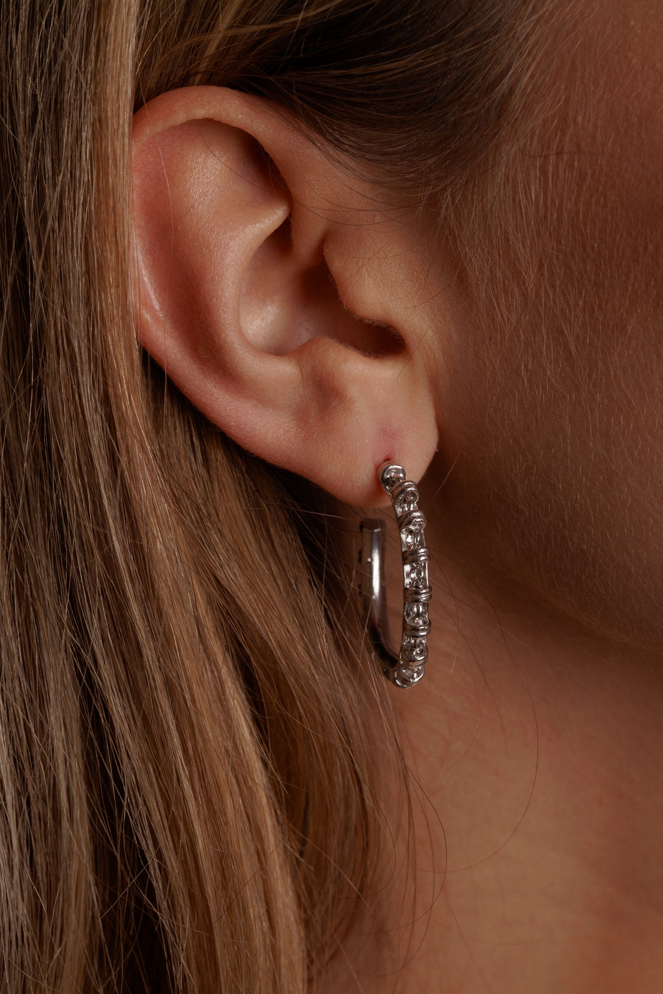 A closeup, side view of a model wearing large silver hoop earrings with a chain design from DelBrenna Italian jewelry design. The earrings are hand-crafted in Tuscany. 