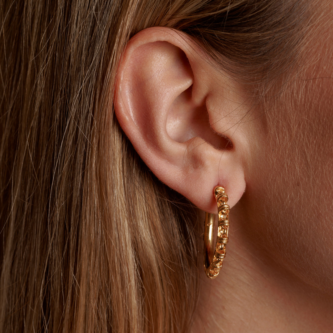 A closeup of a model wearing large gold hoop earrings with a chain design from DelBrenna Italian jewelry design. The earrings are hand-crafted in Tuscany. 