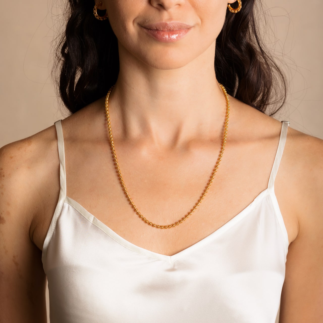 A model wearing a long (20-inch) DelBrenna Iconic Links 3MM gold necklace with matching Links 3MM large gold hoop earrings. Both pieces of hand-crafted Italian jewelry are made by DelBrenna Italian Jewelers in Tuscany. 
